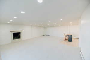 Finished basement with light colored carpet, recessed lighting, a fireplace with flush hearth, a baseboard radiator, and a baseboard heating unit