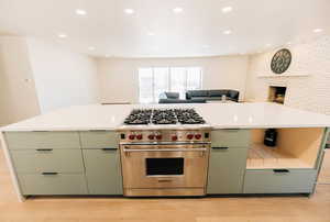 Kitchen featuring green cabinetry, luxury stove, open floor plan, light wood finished floors, and recessed lighting