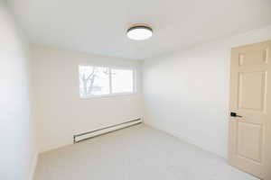 Empty room with baseboard heating and light colored carpet