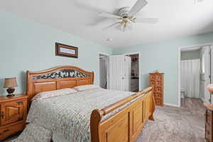 Bedroom with light carpet, a walk in closet, ceiling fan, and connected bathroom