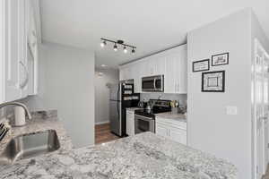 Kitchen featuring white cabinets, stainless steel appliances, light stone countertops, and dark wood-style floors