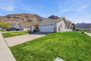 Ranch-style home with a mountain view, an attached garage, concrete driveway, a front lawn, and a residential view