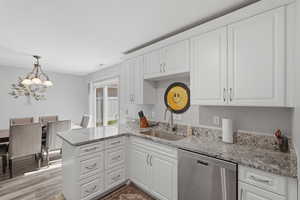 Kitchen featuring stainless steel dishwasher, white cabinets, a peninsula, and light stone counters