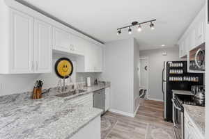 Kitchen featuring stainless steel appliances, white cabinets, light stone countertops, light wood finished floors, and rail lighting