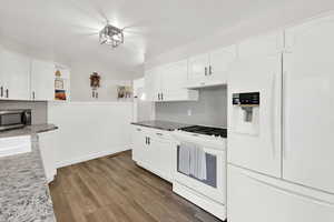 Kitchen with white appliances, dark wood-type flooring, white cabinetry, open shelves, and wainscoting