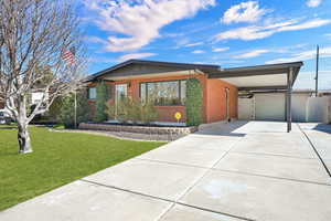 View of front of home with driveway, an attached carport, brick siding, and a front lawn