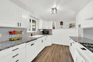 Kitchen with dark stone counters, dishwasher, dark wood-type flooring, white cabinets, and tasteful backsplash