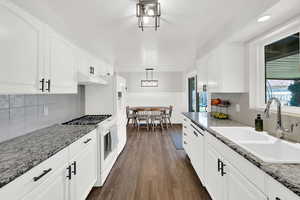 Kitchen with white appliances, backsplash, dark wood-type flooring, and white cabinets