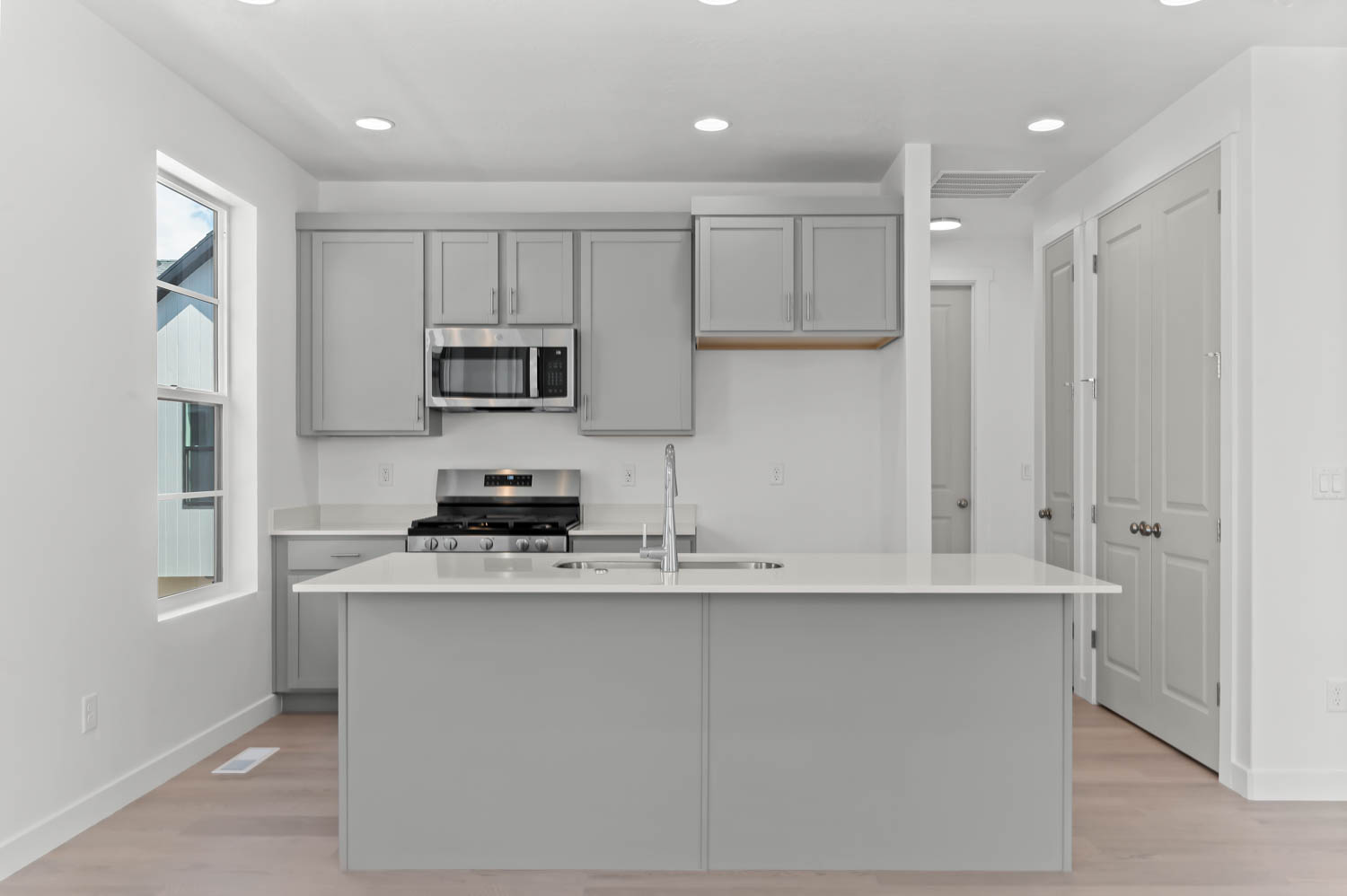 Kitchen with stainless steel appliances, gray cabinetry, a center island with sink, recessed lighting, and light wood-type flooring