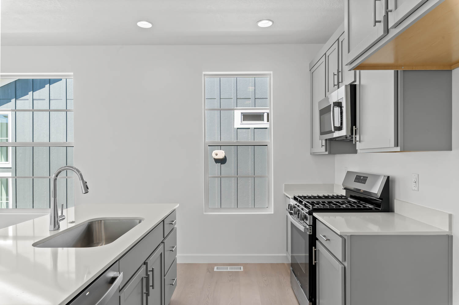 Kitchen featuring gray cabinets, stainless steel appliances, light wood finished floors, light stone countertops, and recessed lighting