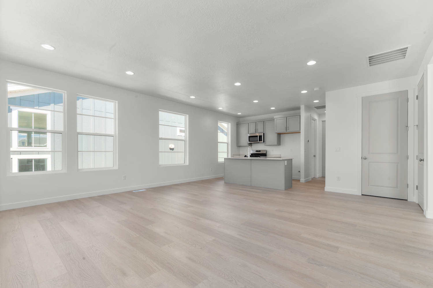 Kitchen featuring open floor plan, a kitchen island with sink, gray cabinets, light wood-style floors, and recessed lighting