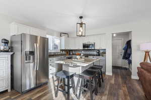 Kitchen with stainless steel appliances, light stone counters, a breakfast bar area, pendant lighting, and white cabinetry