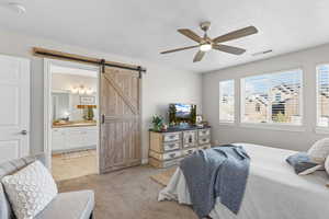 Bedroom featuring a barn door, light carpet, ceiling fan, and ensuite bath
