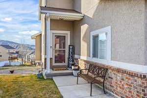 View of exterior entry with stucco siding, a mountain view, and a yard