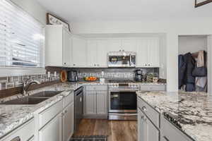 Dual tone kitchen featuring stainless steel appliances, two tone color scheme, dark wood-style flooring, light stone countertops, and tasteful backsplash