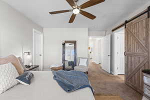 Carpeted bedroom featuring a barn door and ceiling fan