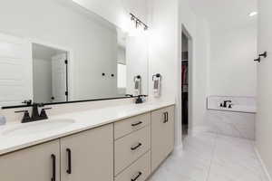 Bathroom with double vanity, a bath, light marble finish flooring, and a walk in closet