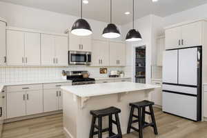 Kitchen featuring stainless steel appliances, a kitchen bar, a kitchen island, light wood finished floors, and decorative light fixtures