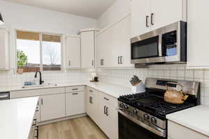 Kitchen with stainless steel appliances, light wood-style floors, white cabinets, decorative backsplash, and light stone countertops