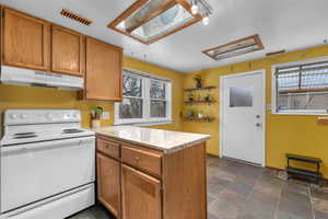 Kitchen featuring white electric range oven, a peninsula, stone finish flooring, wood finish cabinets, and a skylight