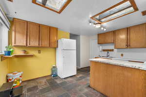 Kitchen with a skylight, freestanding refrigerator, dark stone finish flooring, and wood finish cabinetry