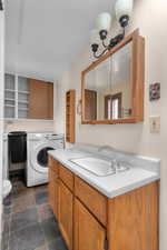 Bathroom featuring washer / dryer, vanity, and dark stone finish flooring