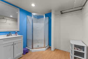 Bathroom with light wood finished floors, vanity, a shower stall, and recessed lighting