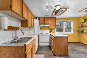 Kitchen featuring a peninsula, white appliances, light countertops, wood finish cabinetry, and a textured ceiling
