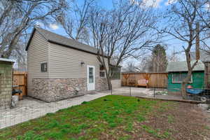 Back of property featuring a patio area, a fenced backyard, stone siding, and a shingled roof