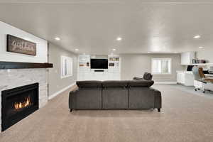 Living area with an office area, light colored carpet, a warm lit fireplace, recessed lighting, and a textured ceiling