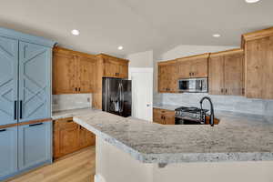 Kitchen with stainless steel appliances, backsplash, wood finish cabinetry, a peninsula, and light wood-style floors