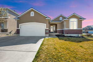 View of front facade featuring brick siding, concrete driveway, stucco siding, a yard, and a garage