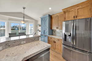 Kitchen with stainless steel appliances, tasteful backsplash, hanging light fixtures, light wood-type flooring, and light stone counters