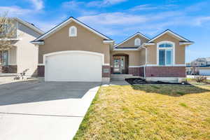 View of front of home with brick siding, concrete driveway, a garage, a front yard, and stucco siding