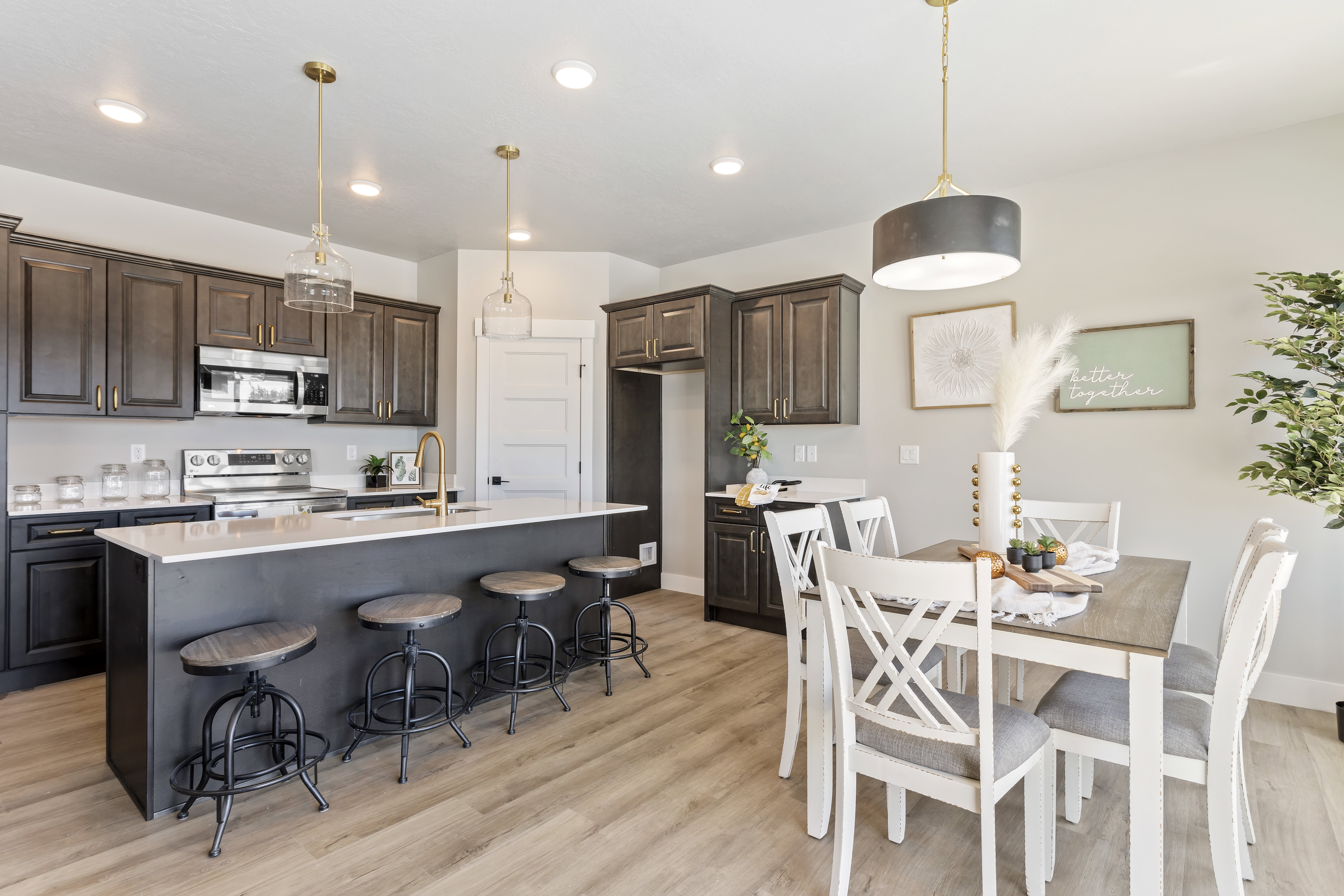 Kitchen with dark wood finish cabinets, stainless steel appliances, light wood-style floors, a center island with sink, and light stone counters
