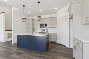 Dual tone kitchen featuring an island with sink, dark wood-style floors, stainless steel appliances, light stone countertops, and two tone cabinetry