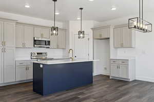 Kitchen with stainless steel appliances, dark wood-style flooring, a kitchen island with sink, light stone countertops, and dual tone cabinetry