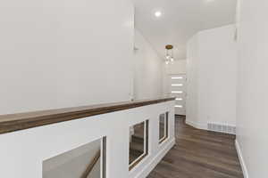 Corridor with dark wood finished floors and suspended lighting
