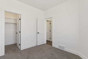 Unfurnished bedroom with dark colored carpet and a spacious closet