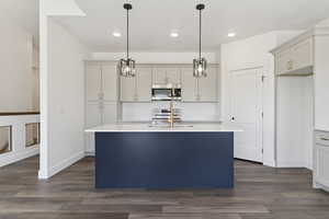 Kitchen featuring stainless steel appliances, dark wood-style floors, an island with sink, decorative light fixtures, and light stone countertops