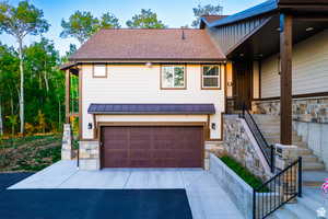 View of front of property with stone siding, a garage, a shingled roof, and driveway