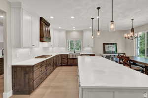 Dual tone kitchen with two tone cabinets, a spacious island, light wood-style flooring, decorative backsplash, and suspended lighting