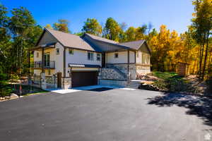 View of front of property with stone siding, driveway, a garage, board and batten siding, and a shingled roof