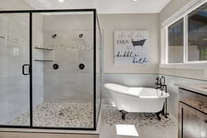 Full bathroom with vanity, a shower stall, a soaking tub, and a wainscoted wall