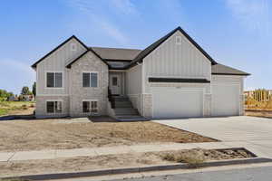 View of front of home with stone siding, board and batten siding, an attached garage, concrete driveway, and roof with shingles