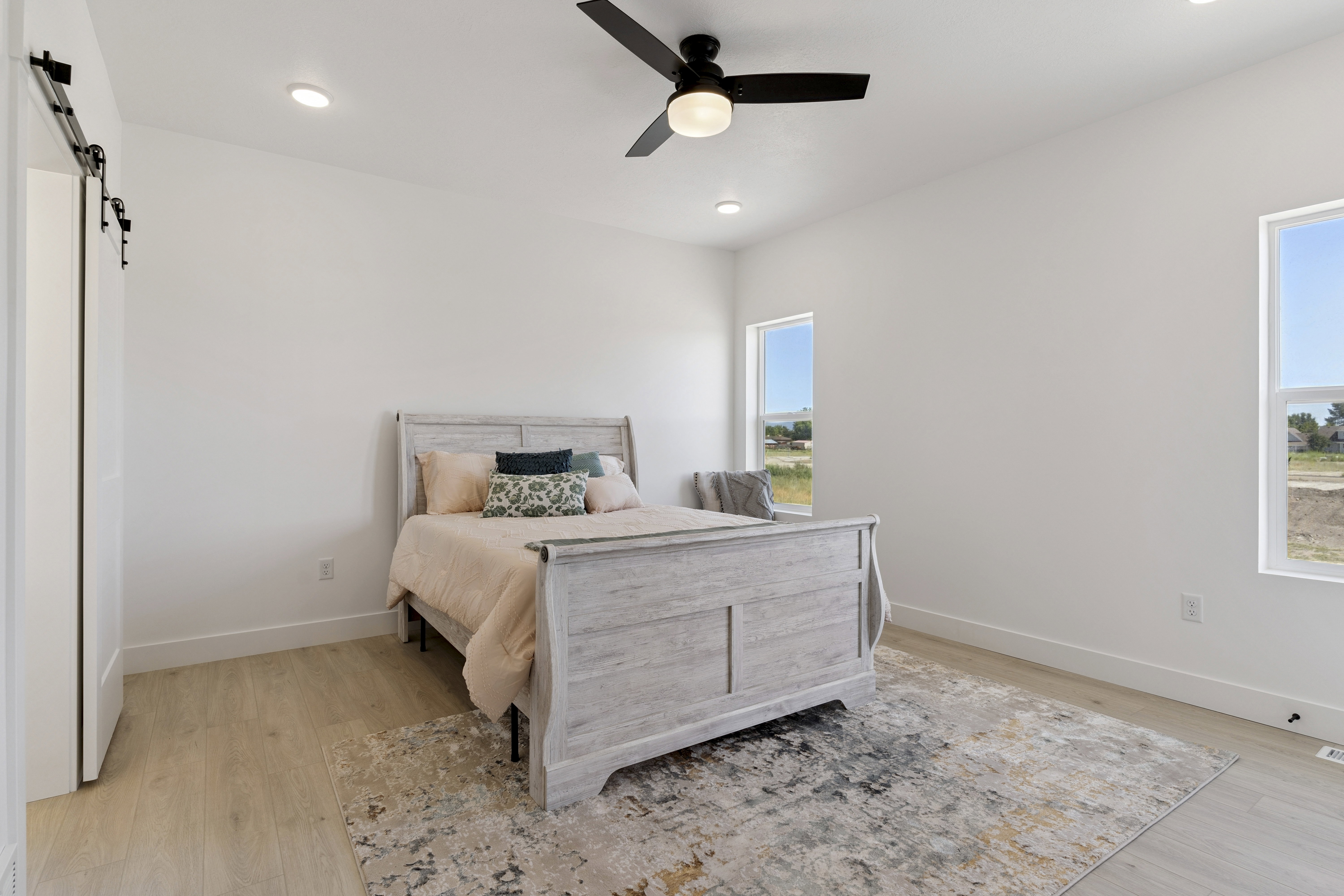 Bedroom with a barn door, light wood-style floors, ceiling fan, and recessed lighting