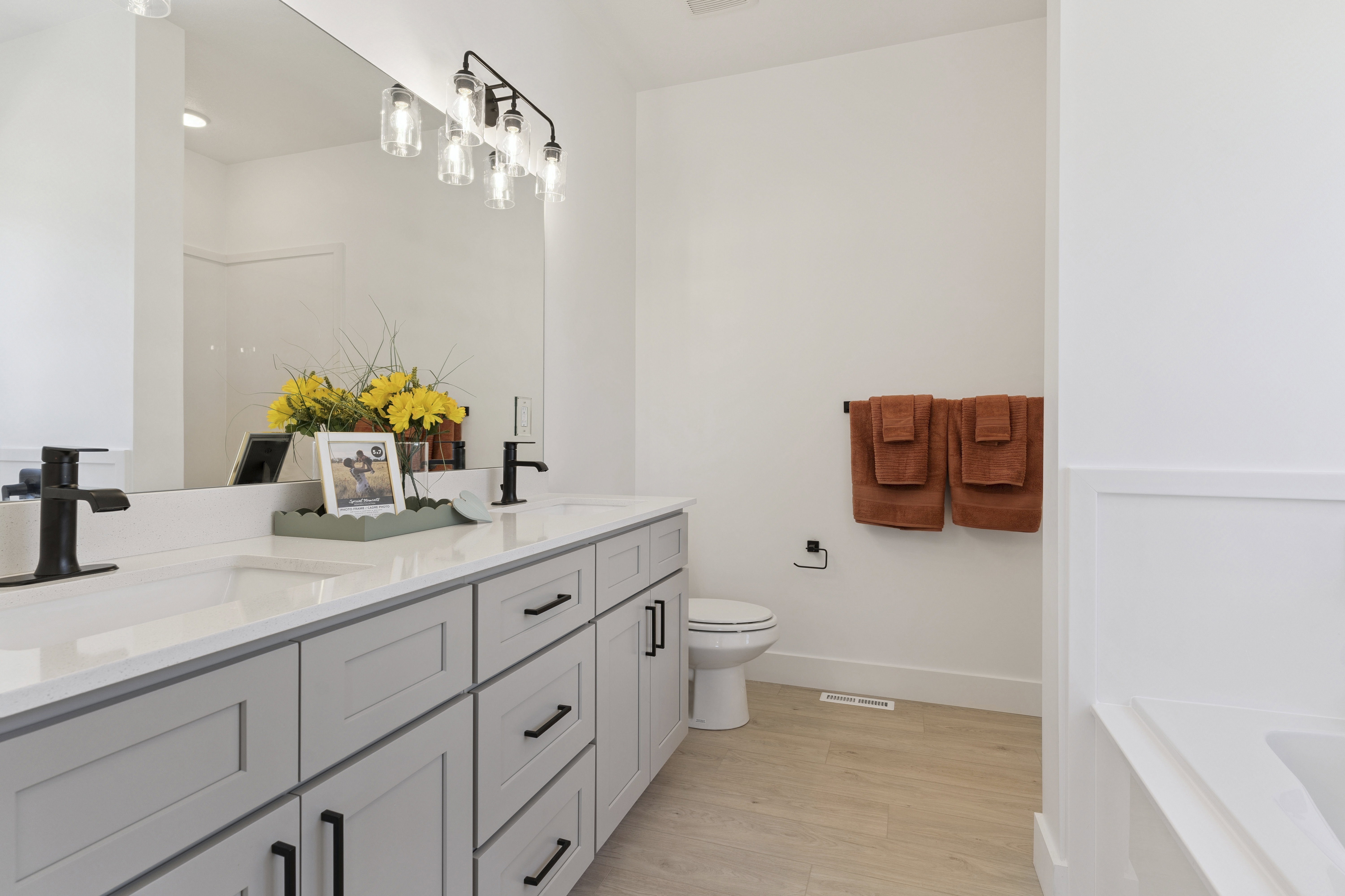 Bathroom featuring double vanity, light wood finished floors, and a bath