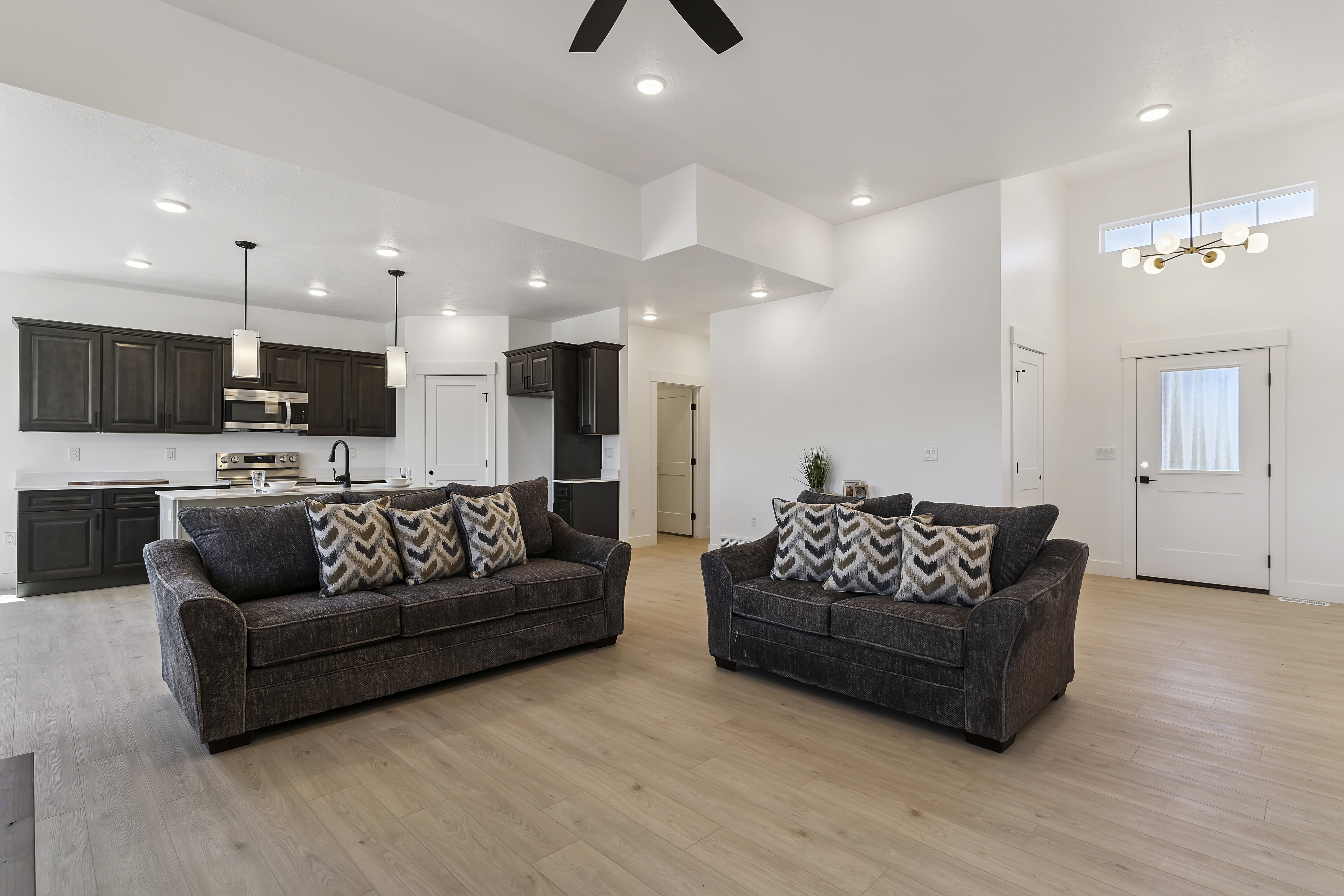 Living room with a ceiling fan, suspended lighting, light wood-style flooring, and a high ceiling