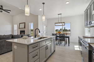 Kitchen featuring gray cabinets, decorative light fixtures, light stone counters, an island with sink, and open floor plan