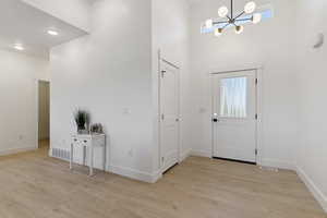 Foyer entrance with a chandelier, light wood-style floors, and a high ceiling